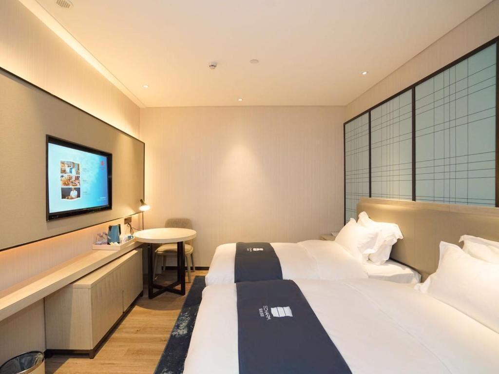 A hotel room with two beds, a desk, a small round table, and a television mounted on the wall.