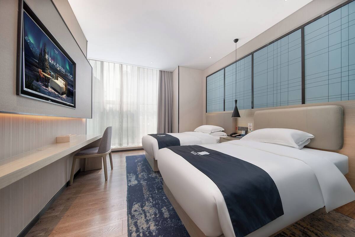 Une chambre d’hôtel avec deux lits, un bureau, une chaise, une télévision et une grande fenêtre.