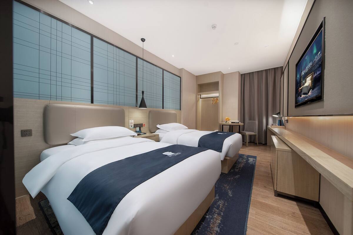 Une chambre d’hôtel avec deux lits, un bureau, une chaise, une télévision et une grande fenêtre donnant sur un beau paysage.