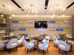A modern dining area with tables and chairs, a large TV screen, and shelves with bottles.