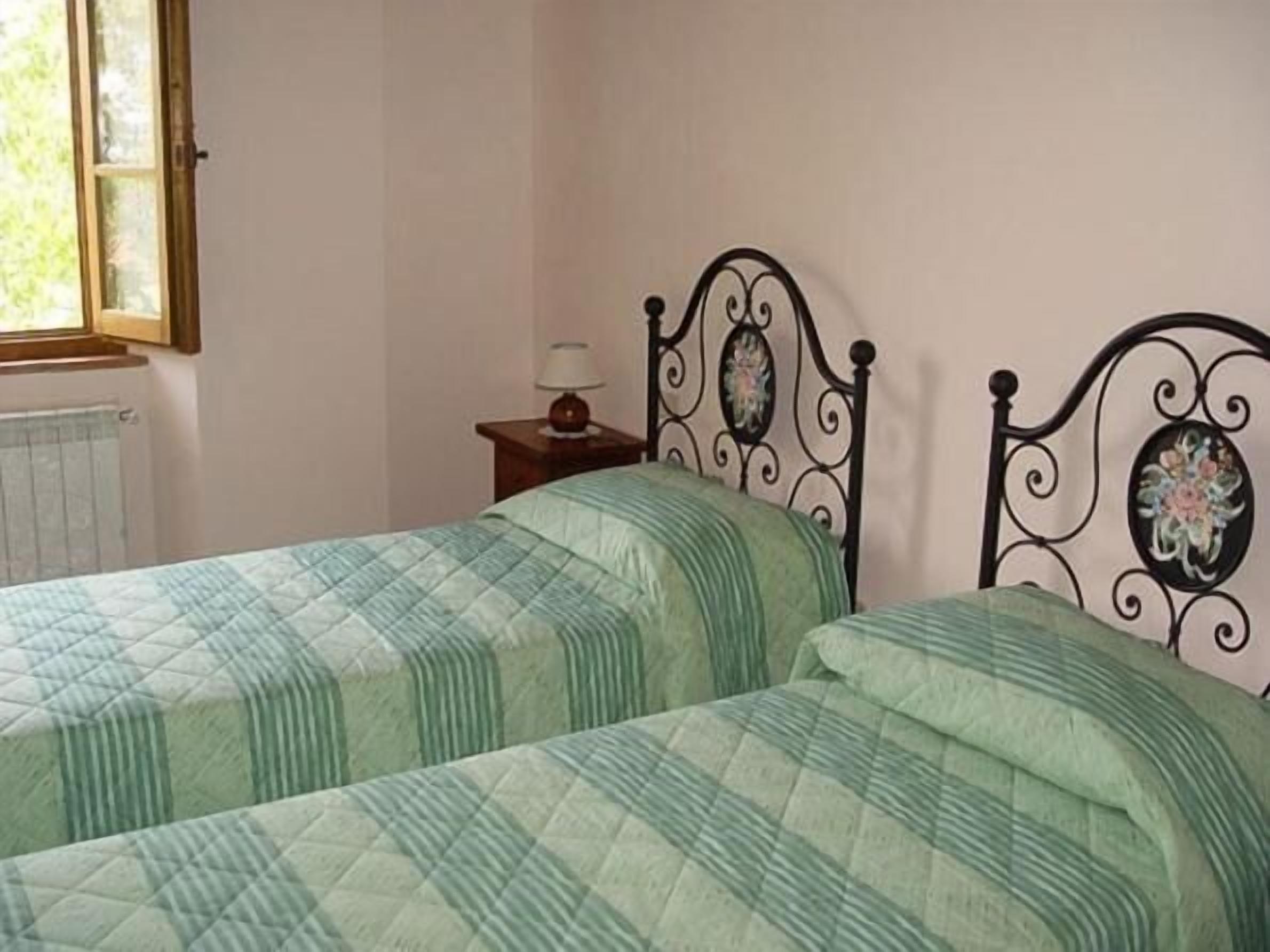 Ein Zimmer mit zwei Betten, einem Heizkörper, einem Fenster und einem Nachttisch mit Lampe.