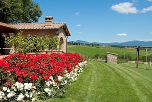 A stone building with a tiled roof, surrounded by a well-maintained lawn and vibrant red and white flowers. - Agriturismo Antico Fio (Poppi)
