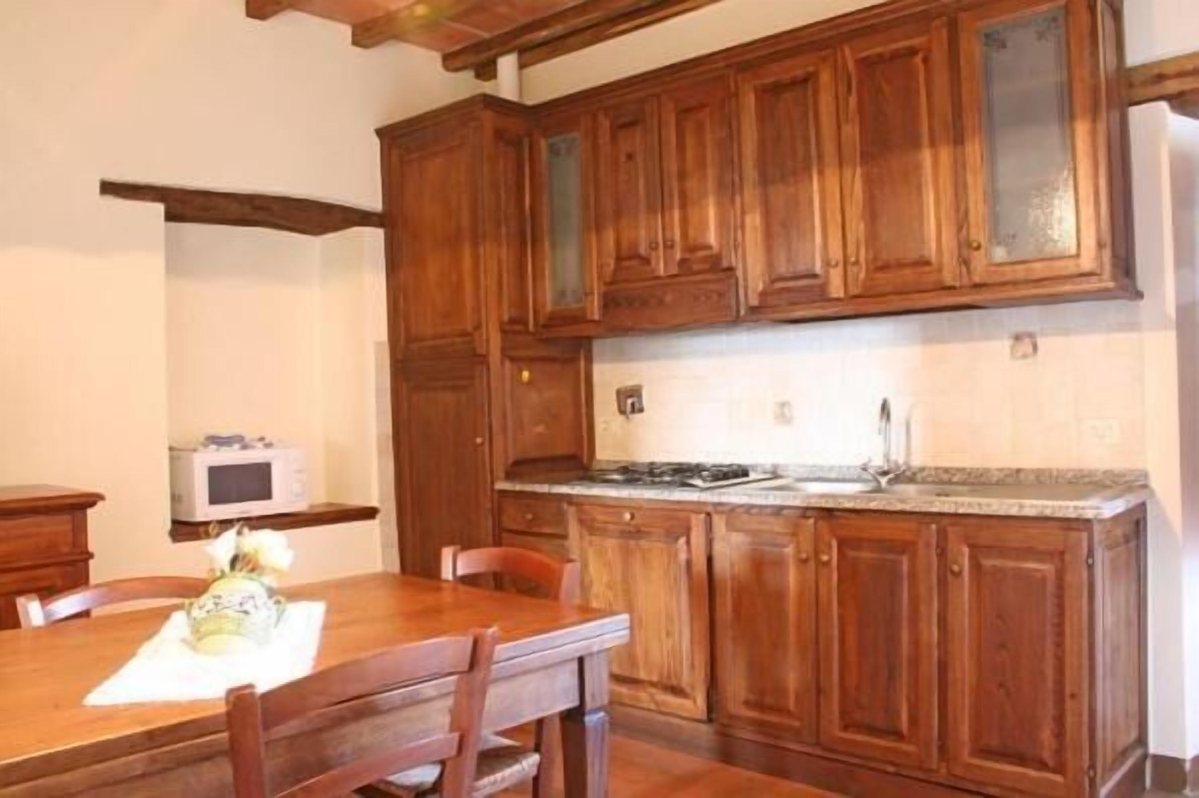 Une cuisine avec des meubles de rangement en bois, un plan de travail en granit et un four à micro-ondes posé sur une étagère.