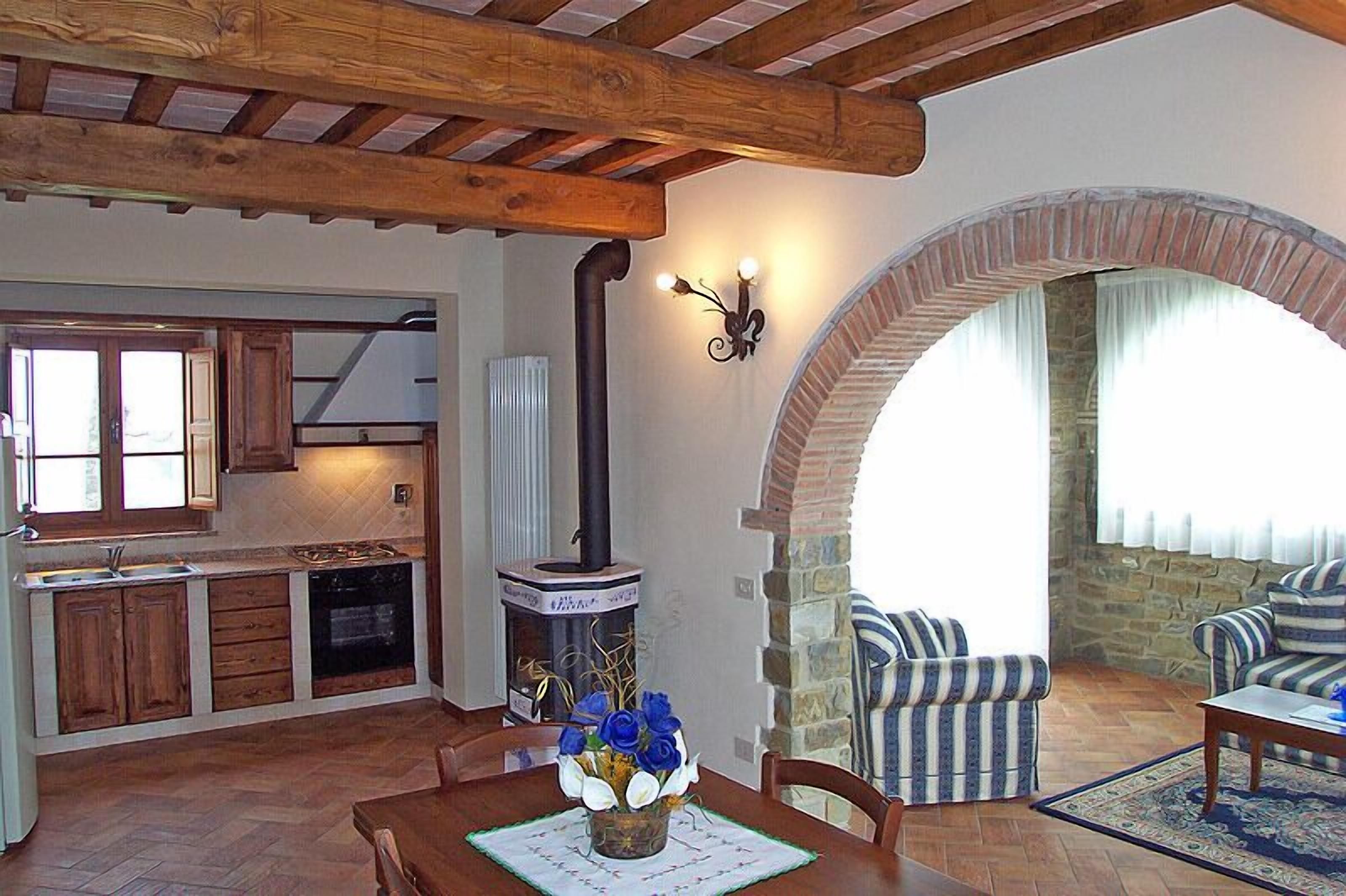 Eine rustikale Küche mit Holzbalken, einem Steinkamin und einem Essbereich mit gestreiften Sofas und einem Tisch.