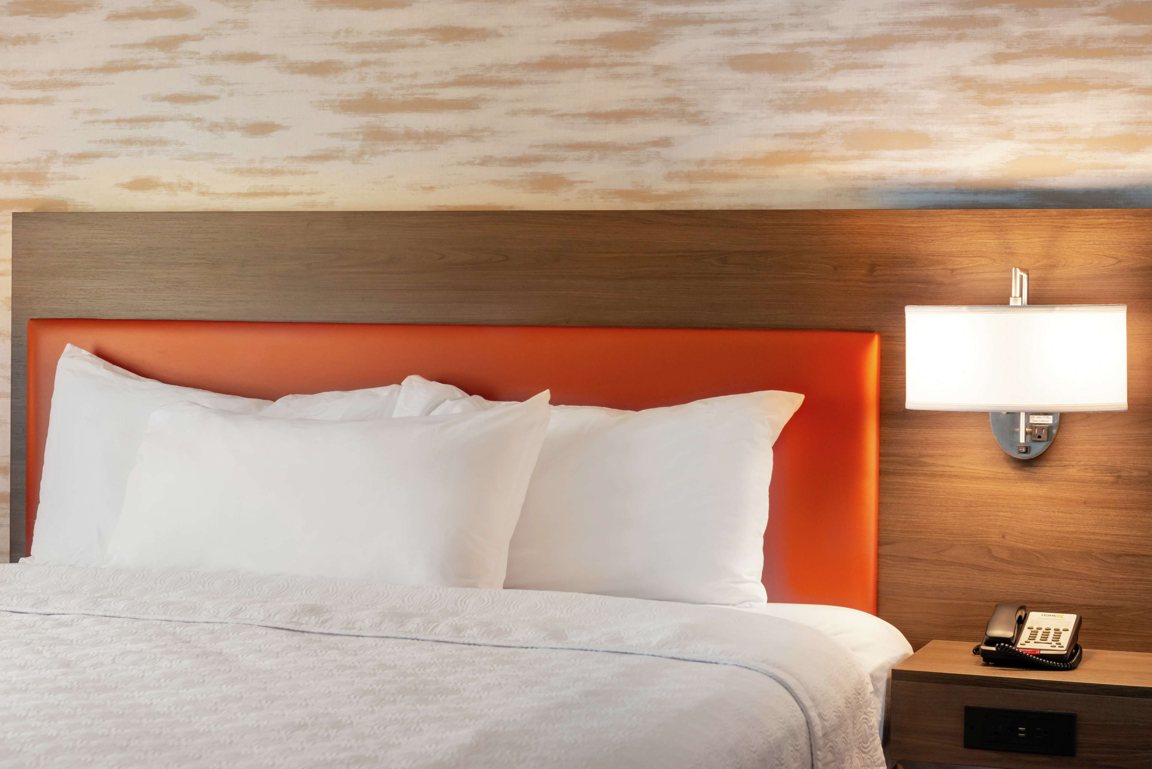Une chambre d’hôtel avec une tête de lit en bois, du linge de lit blanc, une lampe de chevet et un téléphone sur la table de chevet.