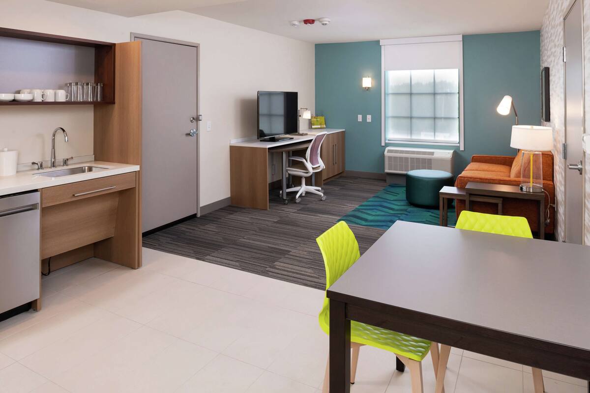 A compact hotel room with a kitchenette, a desk with a computer, a dining table, and a sofa.