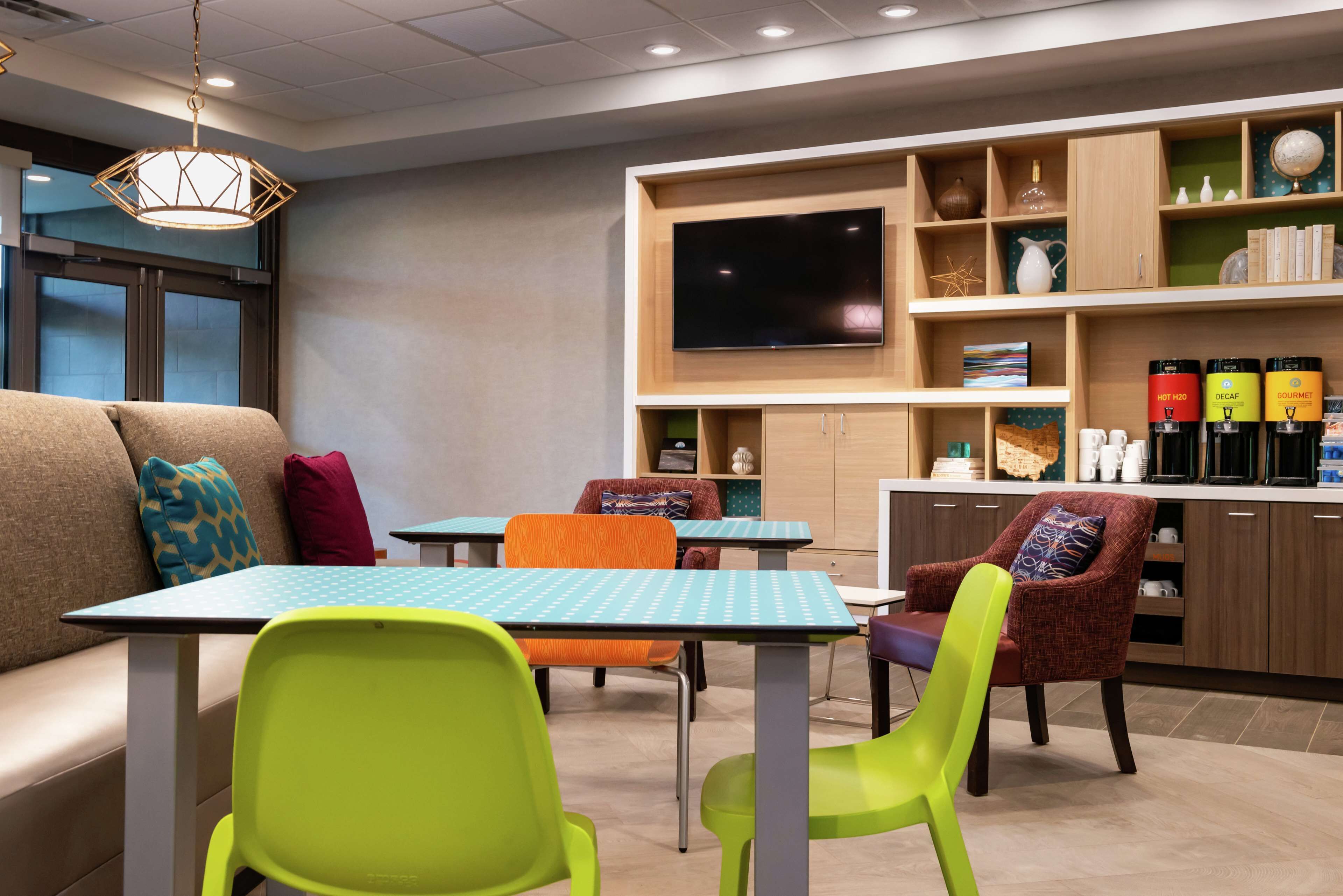 A modern hotel lobby with a sofa, colorful chairs, a flat-screen TV, and a coffee station.