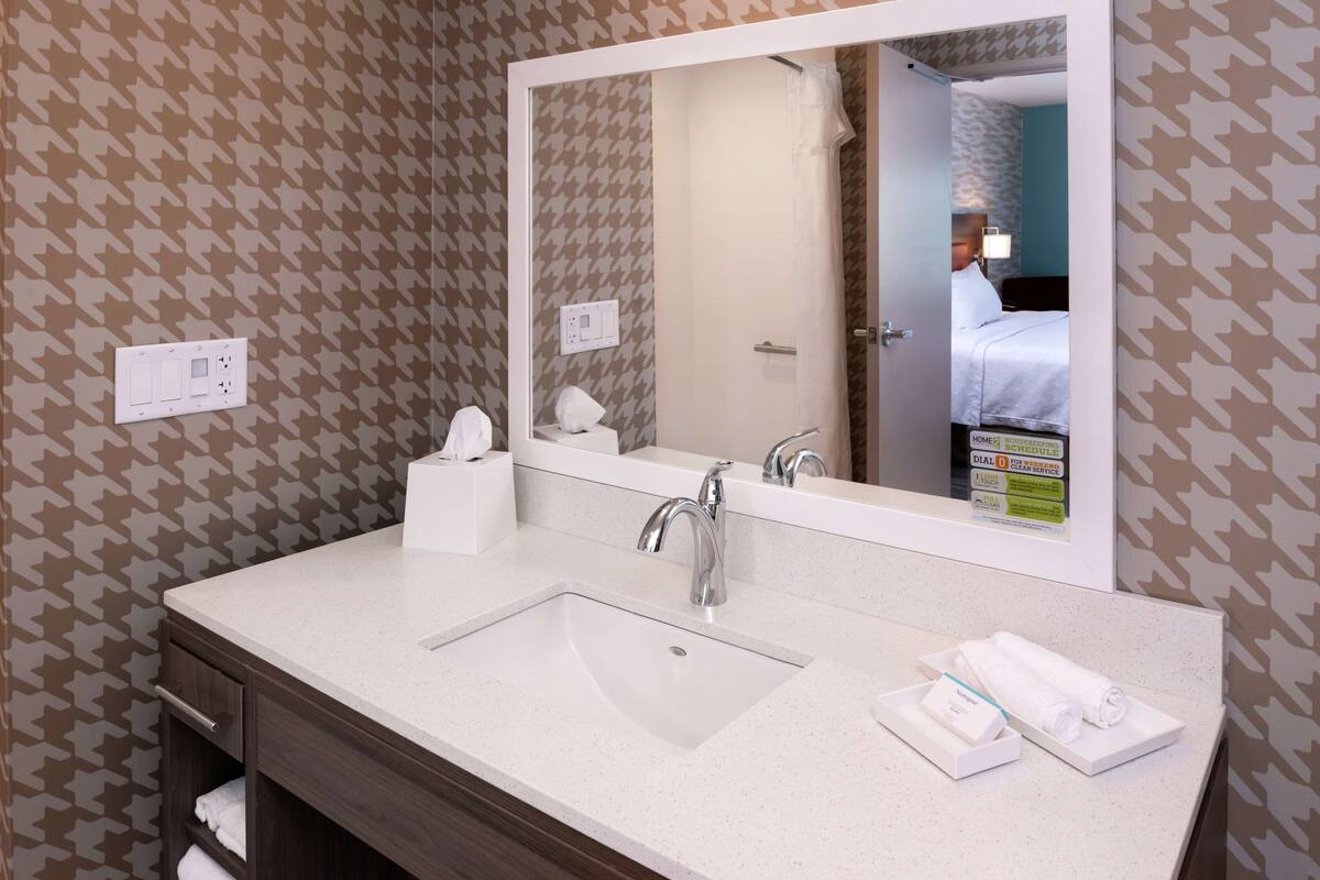 A hotel bathroom with a large mirror, a sink, a towel rack, and a shower curtain.