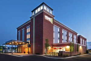 A hotel with a prominent "HOME2" sign, a covered outdoor seating area, and a brick facade.