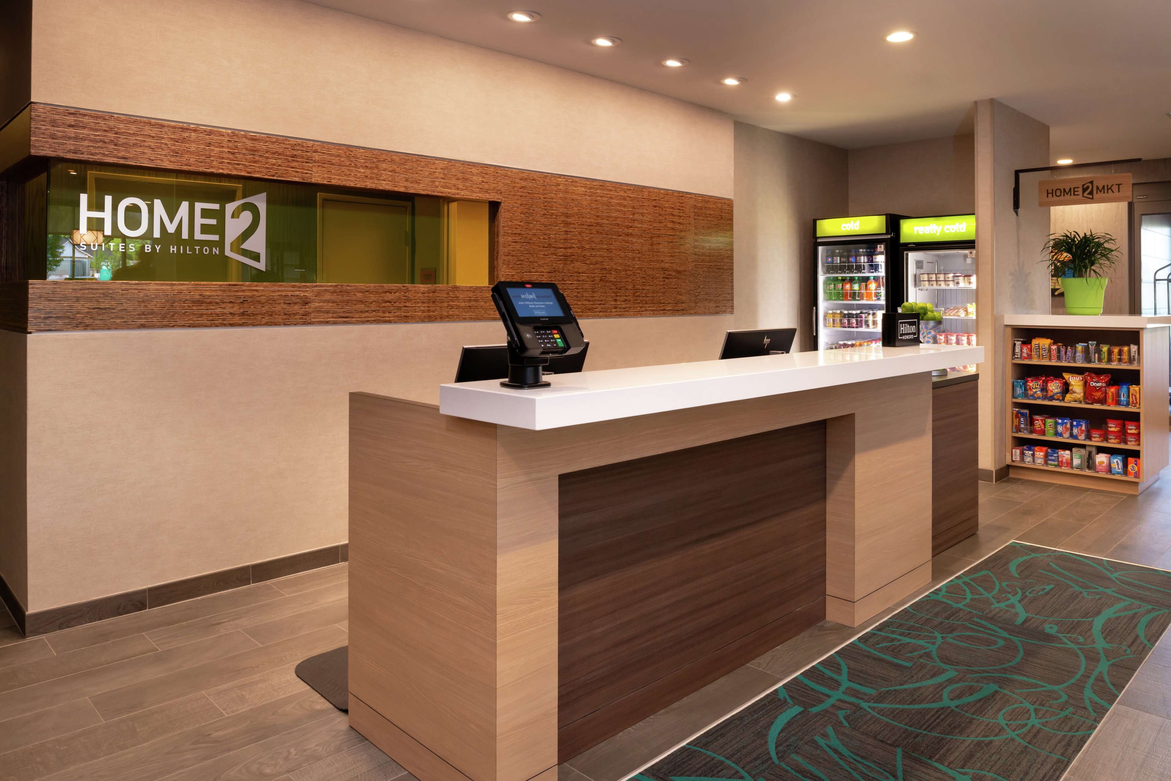 A hotel reception desk with a digital kiosk, a minibar, and a self-service beverage station.
