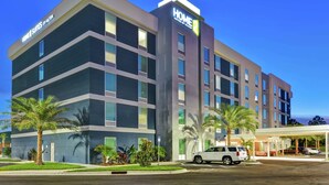 A multi-story hotel with a modern design, featuring a prominent 'HOME' sign, a covered entrance, and a parking area with several cars. - Home2 Suites by Hilton Jacksonville-South/St. Johns Town Ctr (Jacksonville)