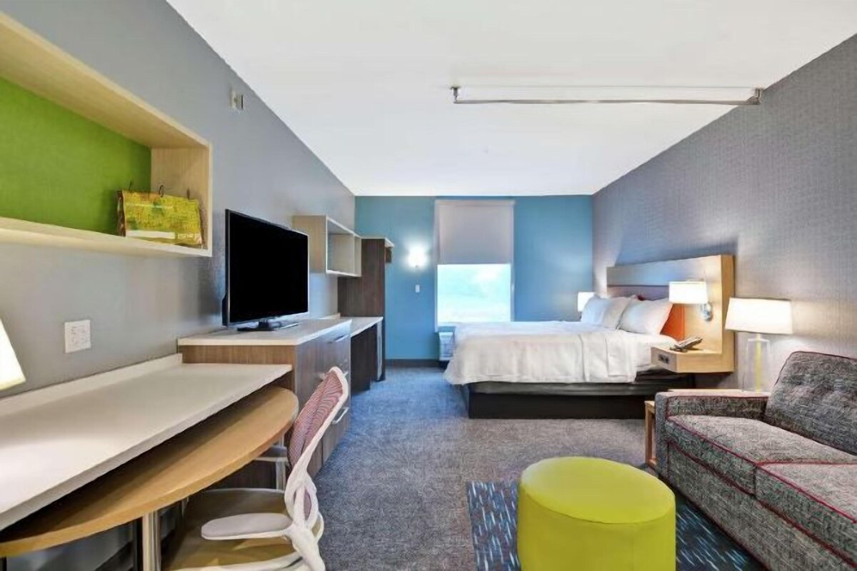 Hotellihuone, jossa on sänky, työpöytä, tuoli, televisio ja sohva.