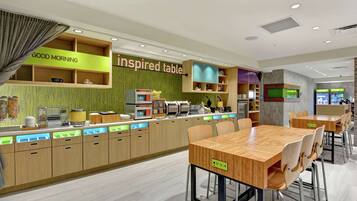 A modern cafe with a green wall, a 'Good Morning' sign, an 'Inspired Table' sign, and a variety of seating options including tables and chairs.