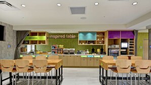 A modern restaurant with a green-themed bar area, wooden tables, and chairs. - Home2 Suites by Hilton Jacksonville-South/St. Johns Town Ctr (Jacksonville)