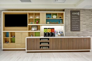 A modern hotel lobby with a large flat-screen TV, a coffee station, and a sign stating 'HOME2 GUARANTEE'. - Home2 Suites by Hilton Jacksonville-South/St. Johns Town Ctr (Jacksonville)