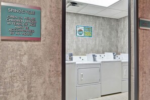 A laundry area with a sign indicating Spin2Cycle is open 24 hours, children under 18 must be accompanied by an adult, and a notice about missing items being taken to the front desk. - Home2 Suites by Hilton Jacksonville-South/St. Johns Town Ctr (Jacksonville)