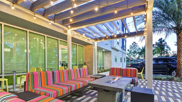 An outdoor seating area with colorful striped sofas and a fire pit table. - Home2 Suites by Hilton Jacksonville-South/St. Johns Town Ctr (Jacksonville)
