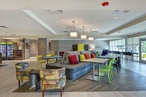A modern interior with a seating area, tables, and a vending machine. - Home2 Suites by Hilton Jacksonville-South/St. Johns Town Ctr (Jacksonville)