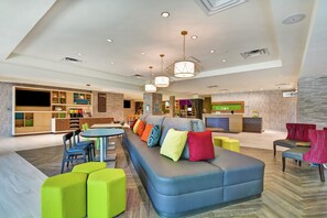 A modern hotel lobby with a seating area, a reception desk, and a kitchenette. - Home2 Suites by Hilton Jacksonville-South/St. Johns Town Ctr (Jacksonville)