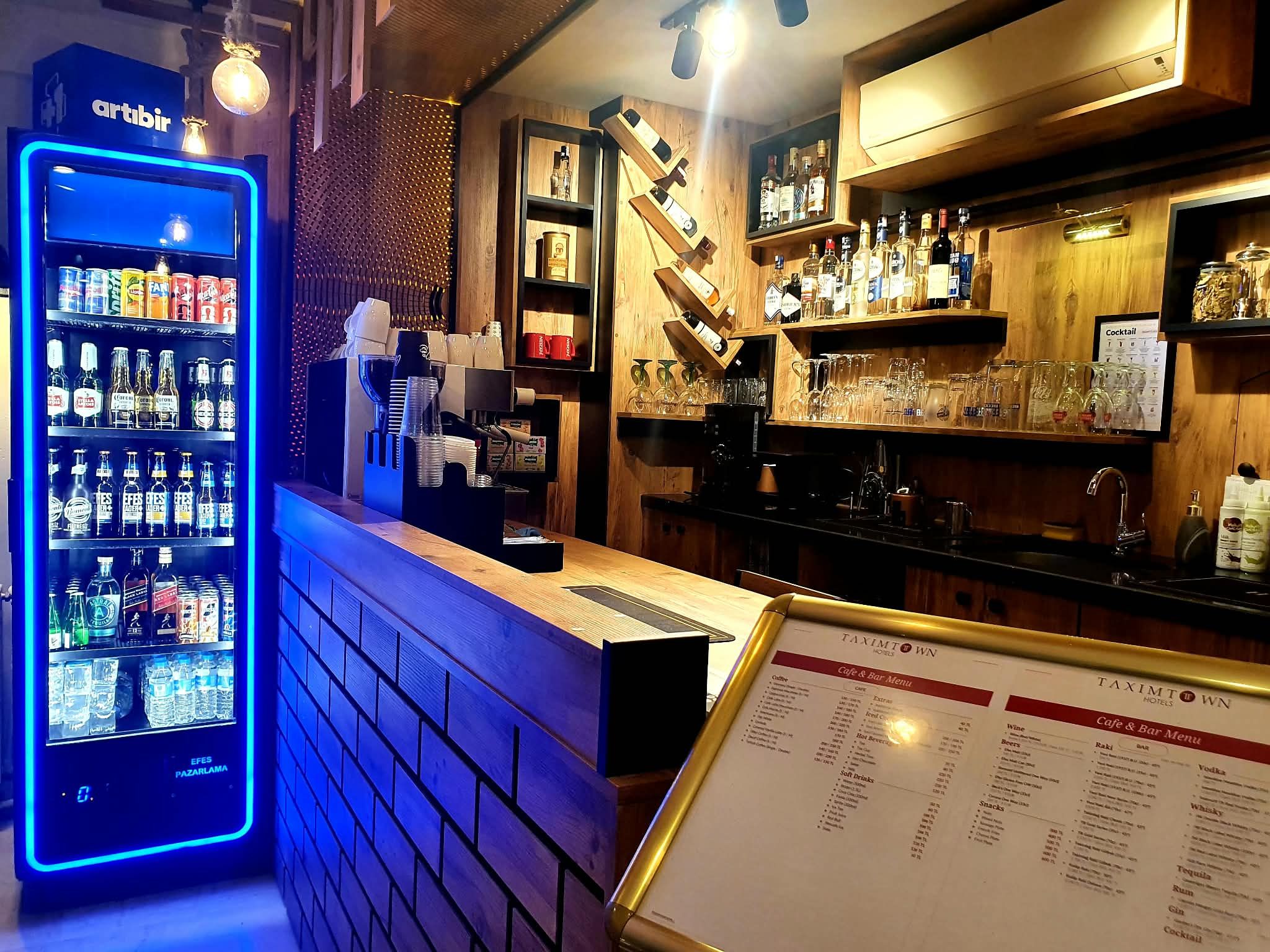 A bar area with a digital drink dispenser, shelves with bottles, and a menu stand.