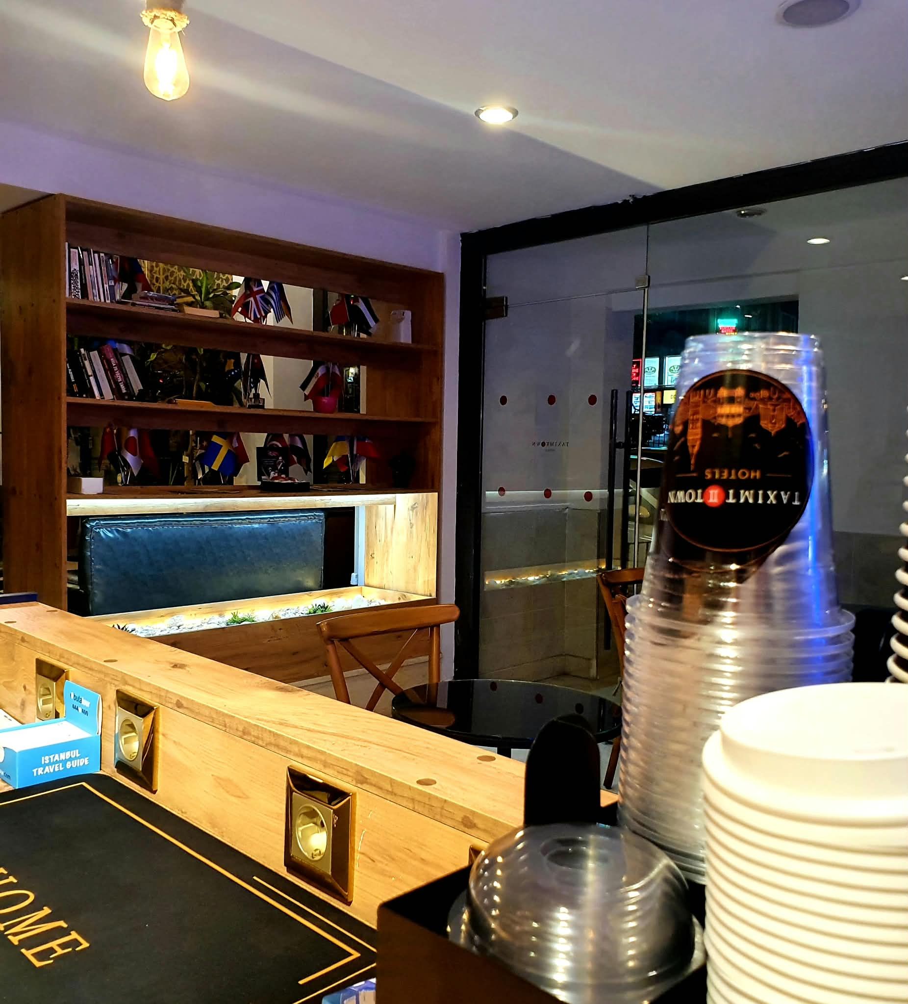 A hotel lobby with a wooden reception desk, a bookshelf with various items, and a large window with a view of the city.