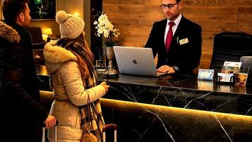 Mostrador de recepción de hotel con una recepcionista, una computadora portátil e invitados con equipaje.