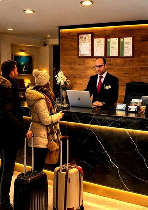 A hotel reception desk with a receptionist, a laptop, and guests with luggage. - Taximtown Hotel (Istanbul)