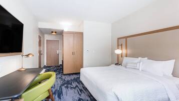 Habitación de hotel con cama, escritorio, silla, televisor y puerta que da a otra habitación.
