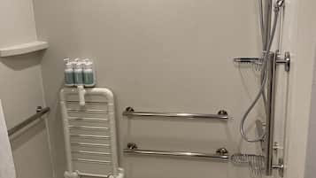 A modern bathroom with a freestanding bathtub, a handheld showerhead, a wall-mounted towel rack, and a shelf with toiletries.