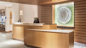 A reception desk with a wooden finish, a modern light fixture, and a decorative wall piece. - Fairfield Inn & Suites Jasper (Jasper)