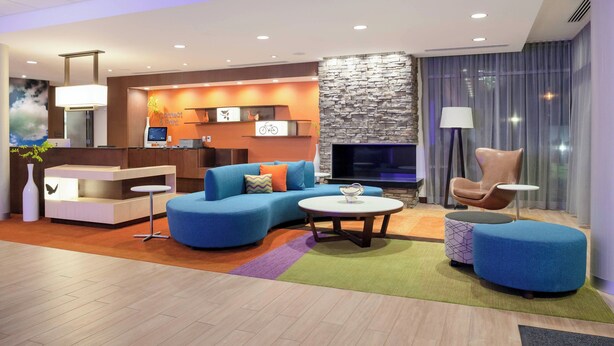 A modern hotel lobby with a blue sofa, a round coffee table, and a stone fireplace. - Fairfield Inn & Suites by Marriott Augusta Washington Rd./I-20 (Augusta)