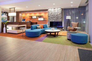 A modern hotel lobby with a blue sofa, a round coffee table, and a stone fireplace. - Fairfield Inn & Suites by Marriott Augusta Washington Rd./I-20 (Augusta)