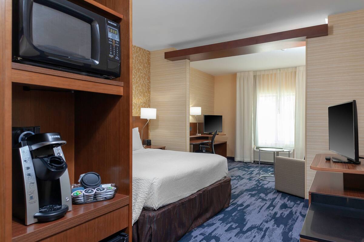 A hotel room with a bed, a desk, a television, a coffee machine, and a microwave.