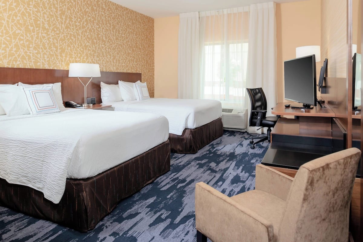 A hotel room with two beds, a desk with a computer, a chair, and a large window with curtains.