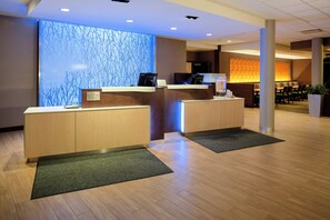 A reception area with two reception desks, a blue wall with a tree pattern, and a seating area with chairs and a table. - Fairfield Inn & Suites by Marriott Augusta Washington Rd./I-20 (Augusta)