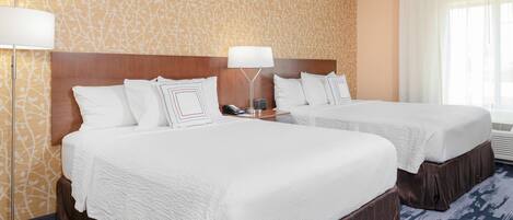 A hotel room with two beds, a wooden headboard, a patterned wall, and a large window with curtains.