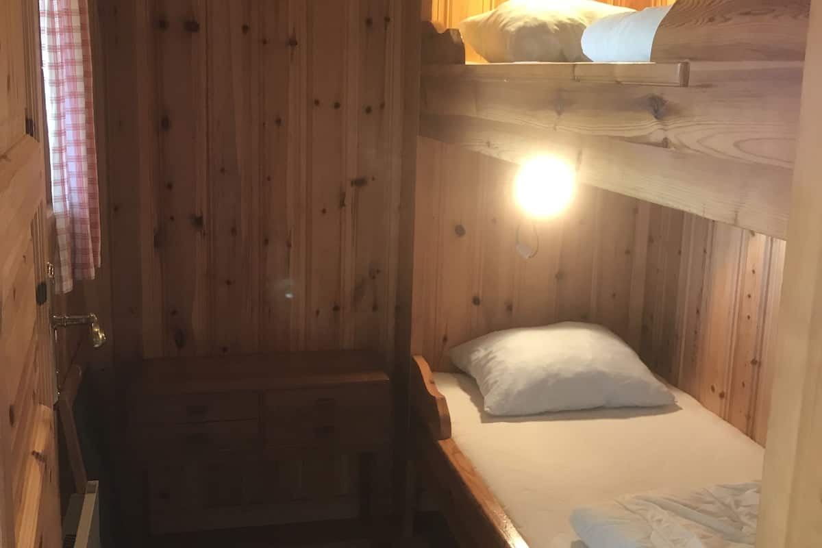 A wooden cabin room with bunk beds, a small bedside table, and a wall-mounted light.