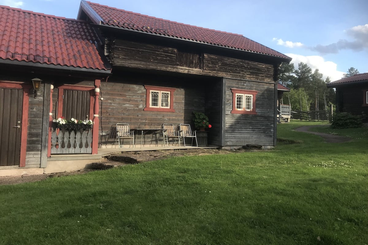 A wooden house with a red-tiled roof, a front porch with metal chairs, and a small garden area.