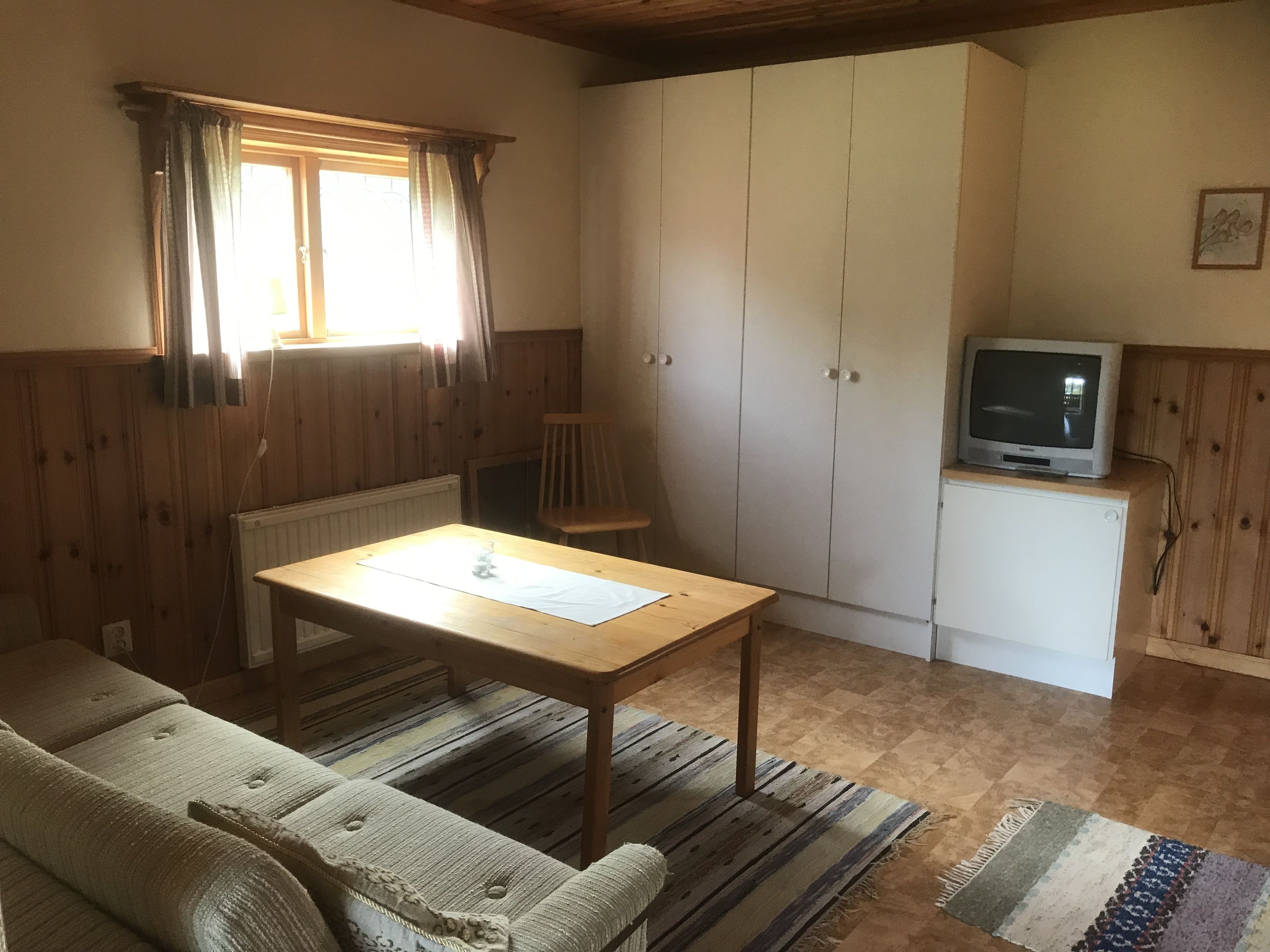 Une pièce chaleureuse avec un plancher en bois, un canapé, une table avec un journal, un téléviseur posé sur un meuble et une armoire.