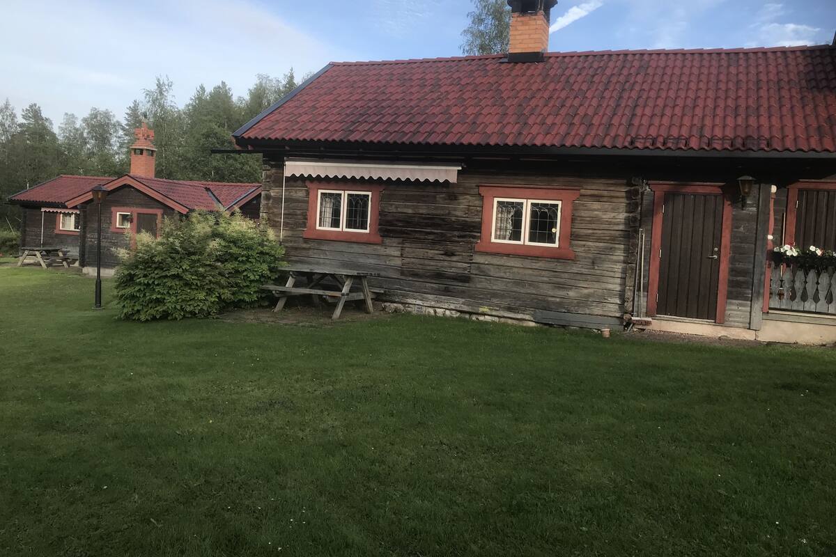 A rustic wooden cabin with a red-tiled roof, a chimney, and a small porch with a bench.