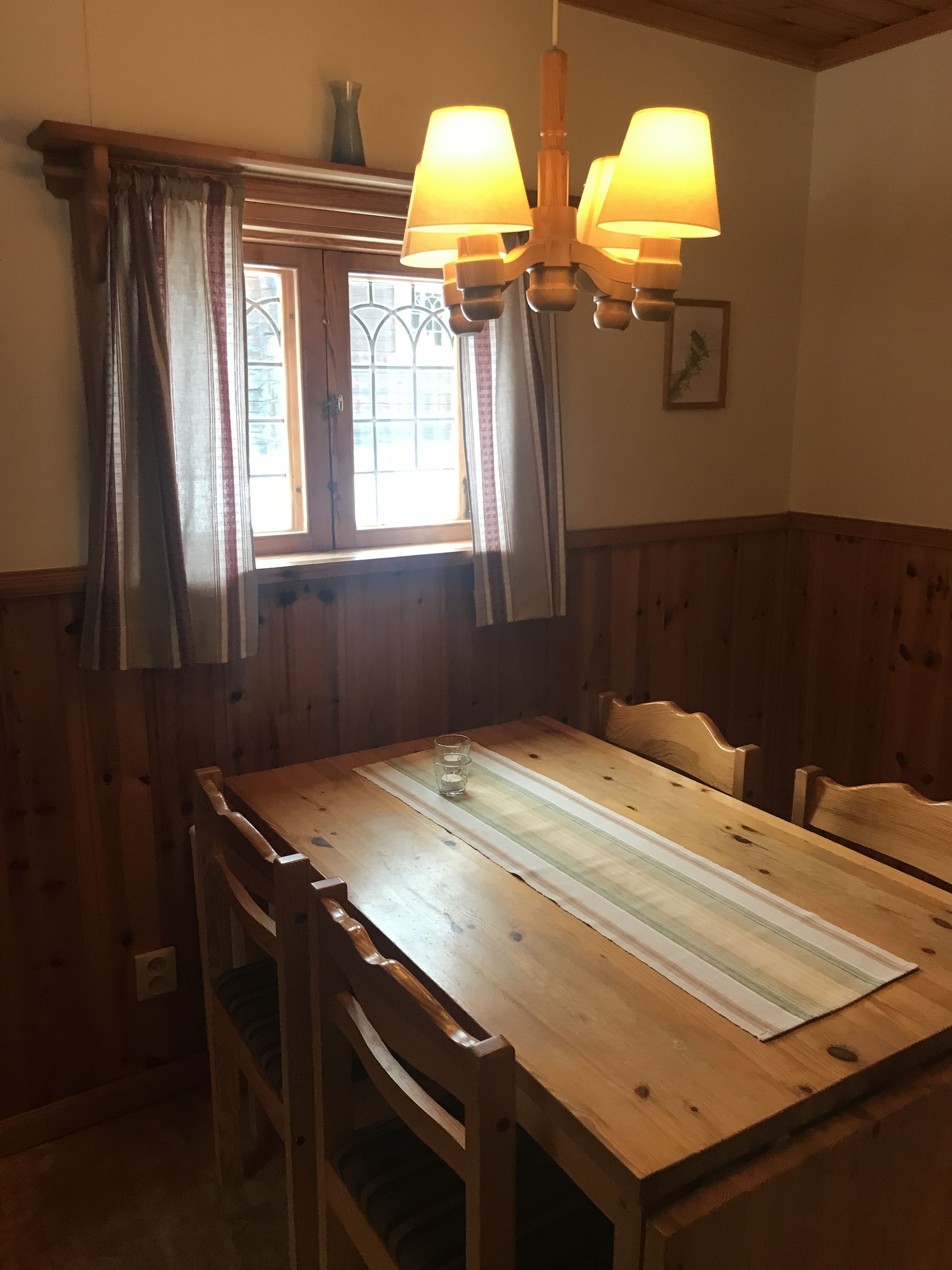A wooden dining table with chairs, a window with curtains, and a chandelier.