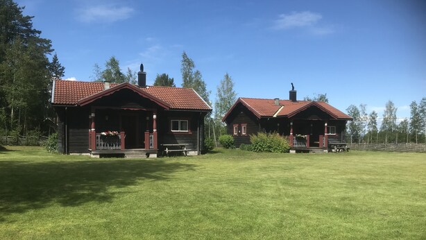 Kaksi puista mökkiä, joissa on punatiilikatto ja edessä vihreä nurmikko.