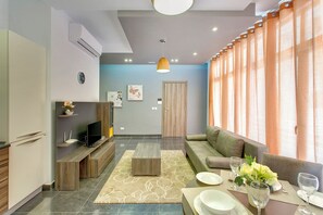 A modern living room with a sofa, TV, and a dining area with a table set for two. - Deluxe Apartment in a Prime Location, Wifi (Sliema)