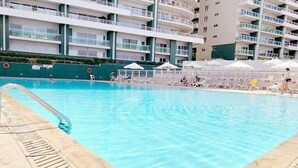 A swimming pool with lounge chairs and umbrellas, surrounded by a multi-story building with balconies. - Fabulous LUX APT inc Pool, Sliema Upmarket Area (Sliema)