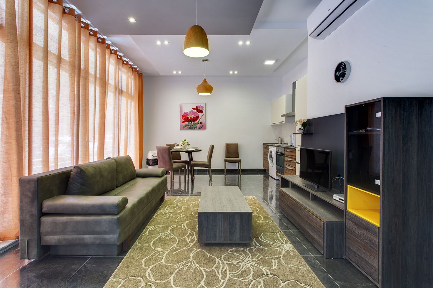 Un salon moderne comprenant un canapé, une table à manger, des chaises, un téléviseur et un coin cuisine avec un lave-linge.