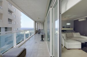 Un balcón con un sofá blanco, una zona de comedor con sillas y vista al mar.