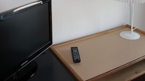 Ein Zimmer mit einem gerahmten abstrakten Gemälde, einem Fernseher, einer Fernbedienung und einer weißen Lampe auf einem Holztisch.