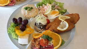Ein Teller mit Speisen, darunter ein paniertes Schnitzel, Salat und weitere Gerichte.
