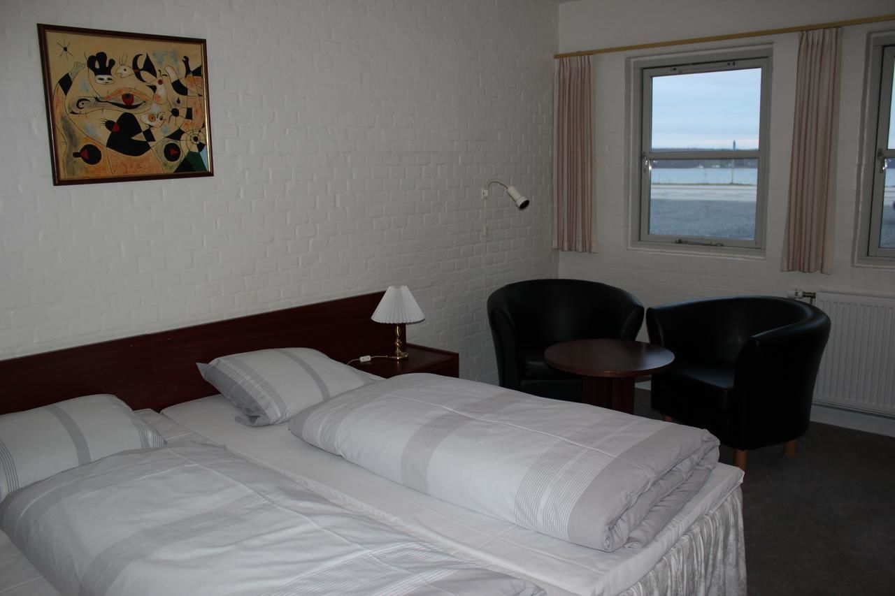 Une chambre d’hôtel avec un lit, une chaise, une table, une lampe et une fenêtre donnant sur la mer.