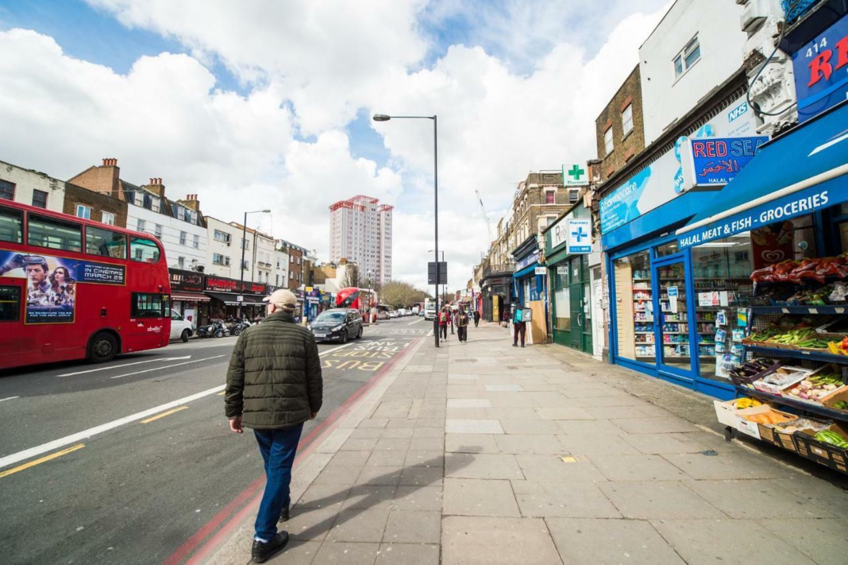 A street scene with a red double-decker bus, a man walking on the sidewalk, and a shop with a blue sign advertising halal meat and fish.